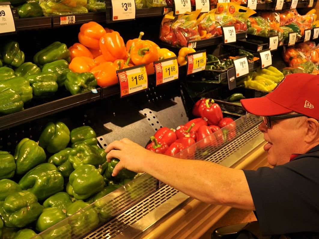 man wearing glasses and baseball cap reaching for pepper in grocery store