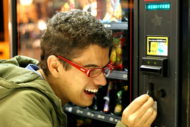 Young adult wearing glasses putting coin in vending machine